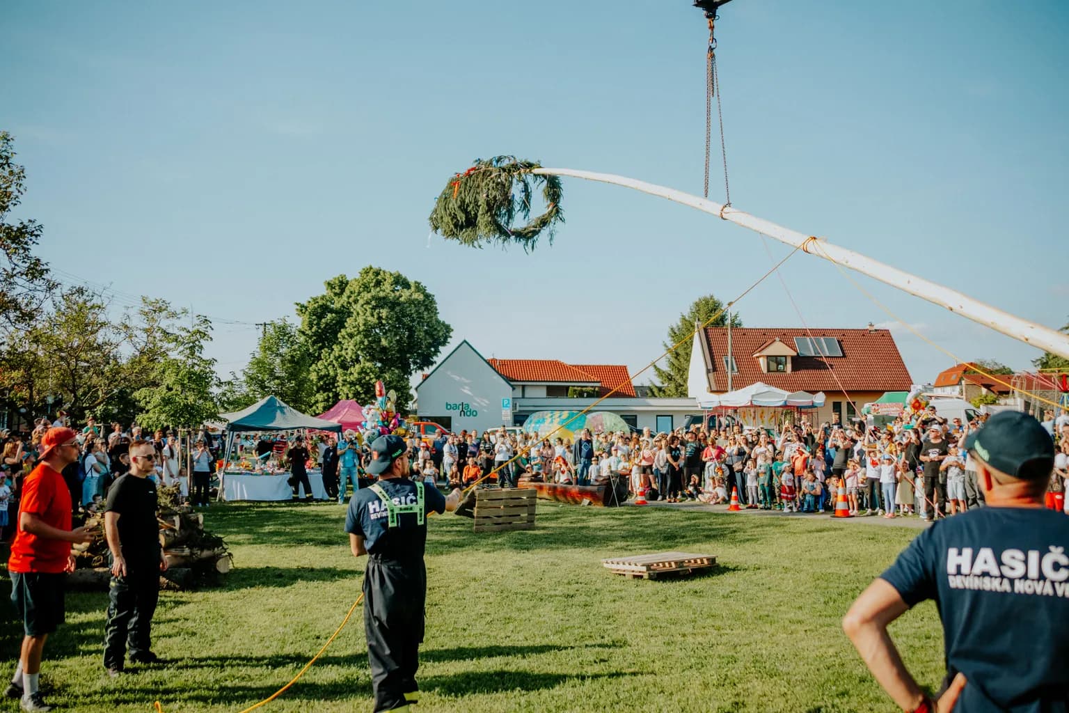 Besucher eines Dorffestes unter freiem Himmel vor Ständen und Bühne